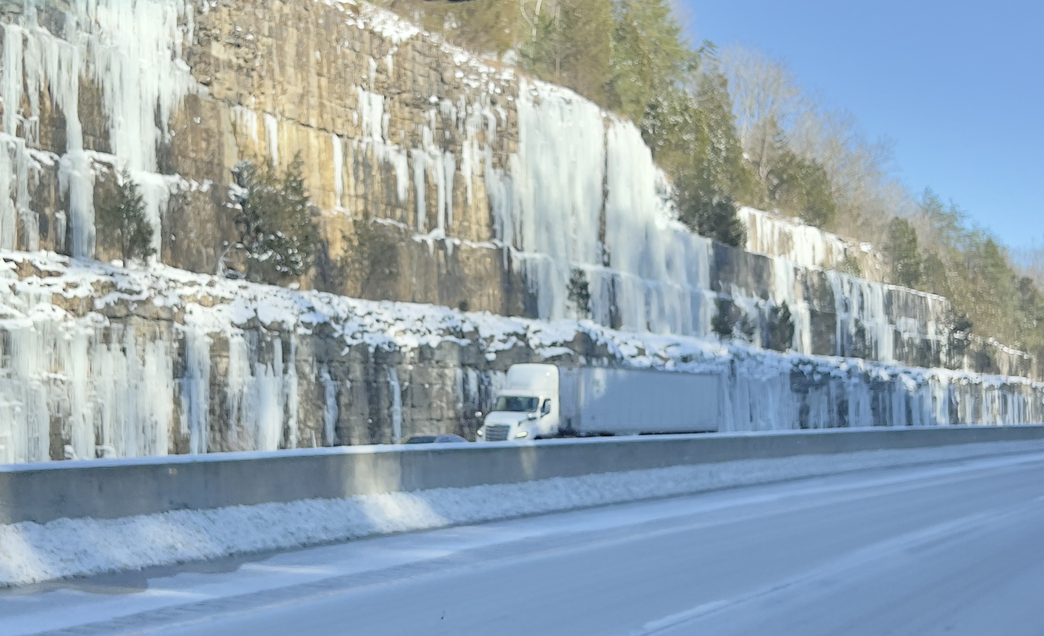 A semi truck driving past a wall of frozen waterfall ice in Orlando, Kentucky