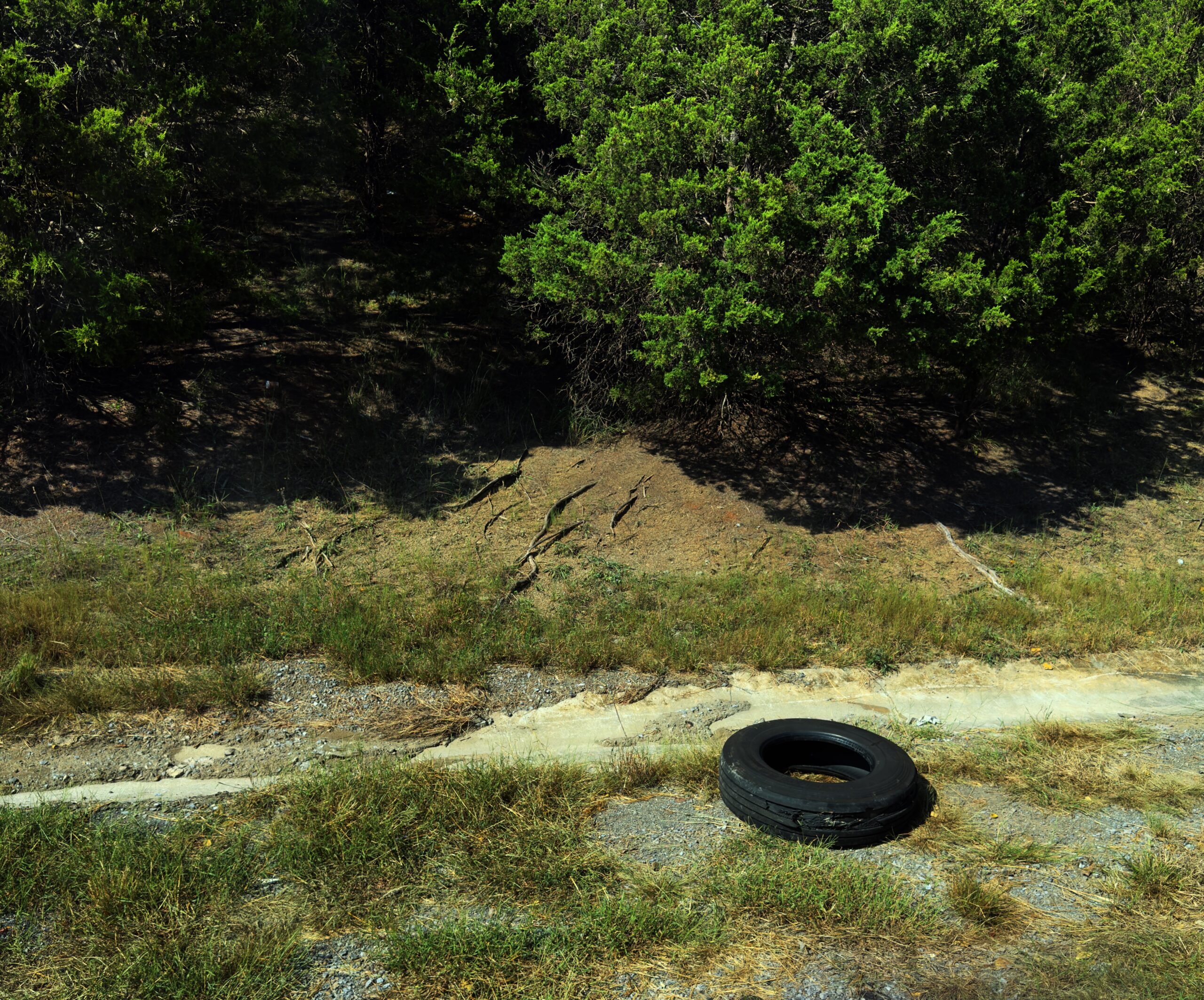 Failed Ralson steer tire with its tread separating, left lying on the gravel shoulder beside a grassy embankment and trees off I-81 in Tennessee